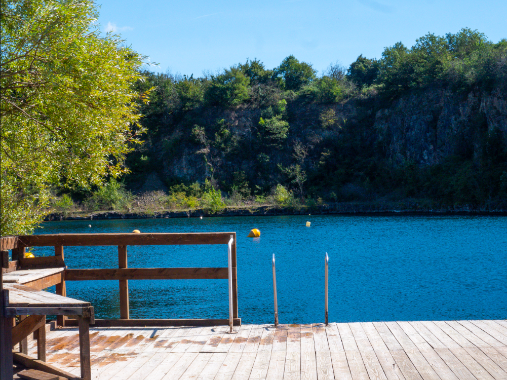 Ponton en bois au bord du plan d'eau turquoise de Chamagnieu, falaise et végétation en arrière-plan
